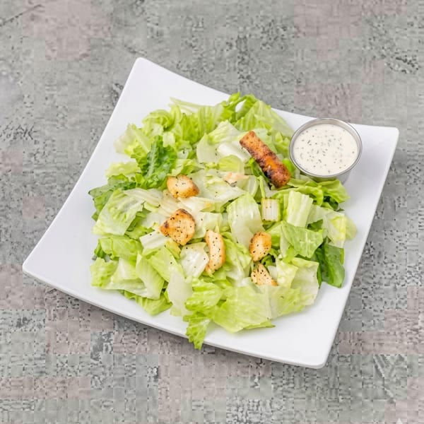 Fresh green salad with croutons and a side of creamy dressing on a white plate.