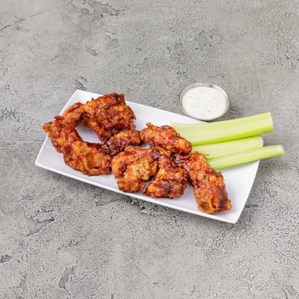 Crispy boneless wings with celery sticks and a side of ranch dressing on a white plate.