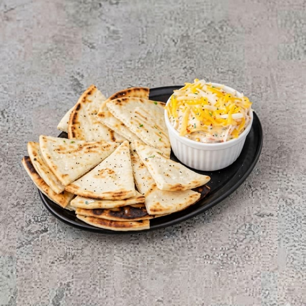 Grilled pita bread triangles with a side of cheesy dip on a black plate.