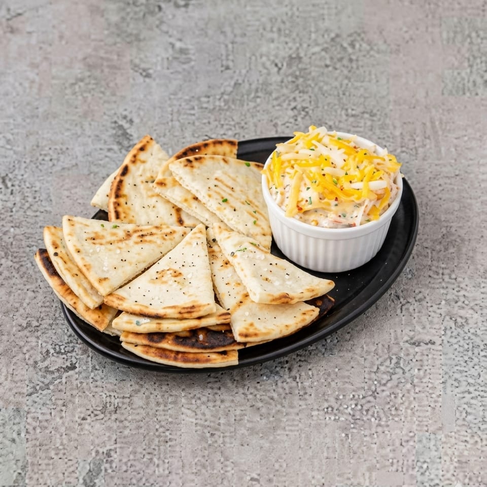 Grilled pita bread triangles with a side of cheesy dip on a black plate.